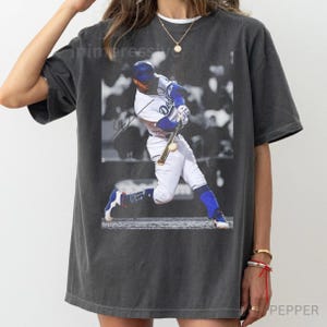 May include: Dark gray t-shirt featuring a black and white image of a baseball player in action. The player is wearing a Dodgers uniform, swinging a bat. The shirt has a vintage, worn look.