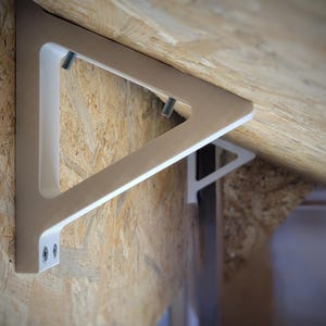 Könnte beinhalten: Ein Paar beige und weiße dreieckige Regalhalterungen an einer Wand mit Holzpaneelen. Die Halterungen bestehen aus einem soliden Material und werden mit Schrauben befestigt. Das Design ist modern und minimalistisch.
