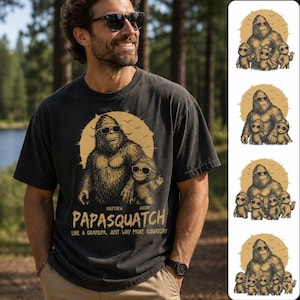 Può includere: T-shirt nera con grafica Bigfoot con occhiali da sole e un Bigfoot più piccolo. Il testo recita "Papasquatch, Like a Grandpa, Just Way More Squatchy." Il design è nei toni del marrone e del beige.