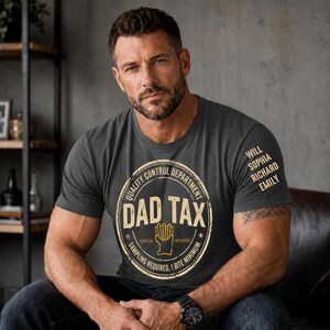 Może przedstawiać: Ciemnoszary t-shirt z okrągłym dekoltem i beżową, okrągłą grafiką z napisem "QUALITY CONTROL DEPARTMENT", "DAD TAX", "CERTIFIED", "AUTHORIZED", "SAMPLING REQUIRED, 1 BITE MINIMUM" oraz ikoną frytki. Na rękawie widnieją imiona "WILL", "SOPHIA", "RICHARD" i "EMILY".