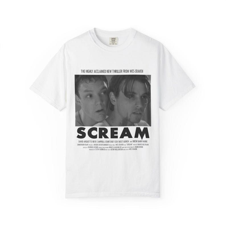 Pu&ograve; includere: T-shirt bianca con un'immagine in bianco e nero del film "Scream". La grafica include il titolo del film e il testo "THE HIGHLY ACCLAIMED NEW THRILLER FROM WES CRAVEN". La maglietta elenca anche i nomi degli attori.