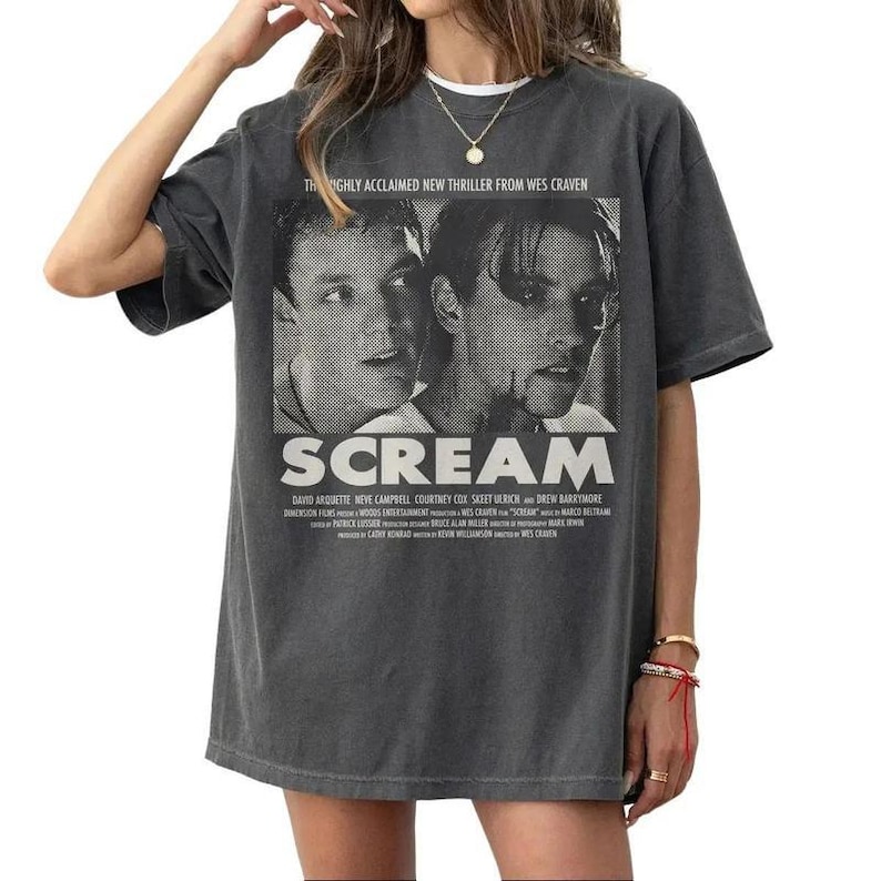 Pu&ograve; includere: T-shirt grigio scuro con un design di locandina del film "Scream". Il design include il titolo del film e le immagini di due attori. La maglietta include anche il testo "HIGHLY ACCLAIMED NEW THRILLER FROM WES CRAVEN."