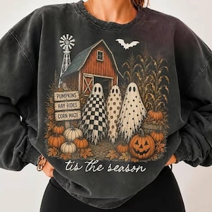Könnte beinhalten: Ein anthrazitfarbenes Sweatshirt mit Rundhalsausschnitt und einem Grafikdruck, der eine rote Scheune, eine Windmühle und drei Geister zeigt. Der Text lautet PUMPKINS, HAY RIDES, CORN MAZE und tis the season. Das Design enthält Kürbisse.