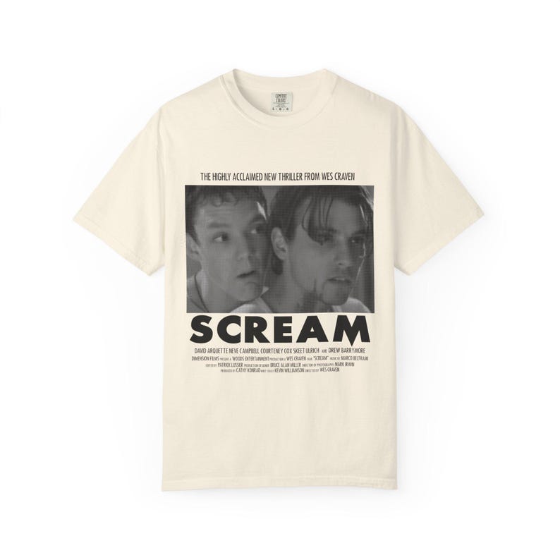 Pu&ograve; includere: T-shirt color crema con immagine in bianco e nero del film "Scream". La grafica include il titolo del film e il testo "THE HIGHLY ACCLAIMED NEW THRILLER FROM WES CRAVEN". Sotto il titolo sono elencati i nomi degli attori.
