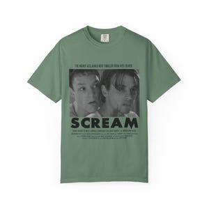 Pu&ograve; includere: T-shirt verde salvia con un'immagine in bianco e nero del film "Scream". L'immagine mostra due attori e il titolo del film in lettere nere in grassetto. Il testo "THE HIGHLY ACCLAIMED NEW THRILLER FROM WES CRAVEN" &egrave; sopra l'immagine.