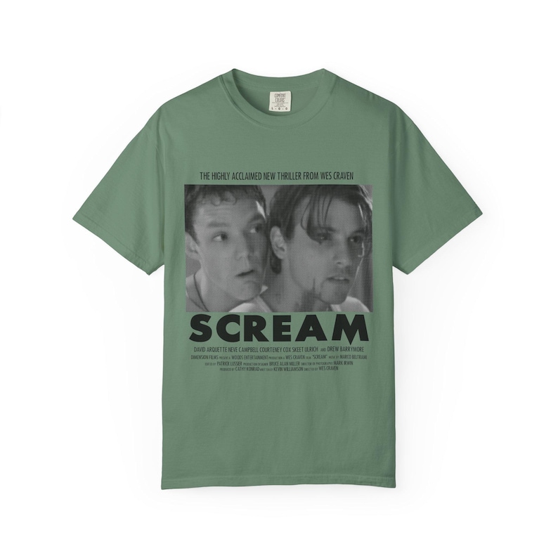 Pu&ograve; includere: T-shirt verde salvia con un'immagine in bianco e nero del film "Scream". L'immagine mostra due attori e il titolo del film in lettere nere in grassetto. Il testo "THE HIGHLY ACCLAIMED NEW THRILLER FROM WES CRAVEN" &egrave; sopra l'immagine.