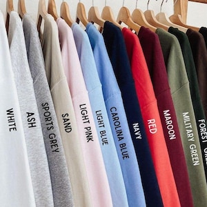 Pu&ograve; includere: Un'esposizione di felpe di vari colori appese a grucce di legno. I colori includono bianco, cenere, grigio sportivo, sabbia, rosa chiaro, azzurro, Carolina blu, blu navy, rosso, bordeaux, verde militare, verde foresta, cioccolato fondente e nero. Ogni felpa ha un'etichetta di colore.