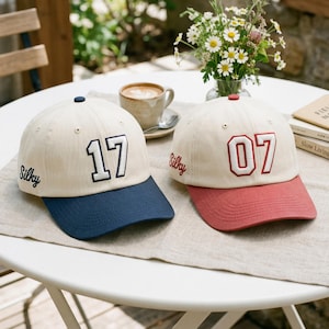 May include: Two baseball caps with cream-colored crowns and navy blue and red brims. One cap has the number "17" in navy blue and the word "Silky" embroidered in navy blue. The other cap has the number "07" in red and the word "Silky" embroidered in red.