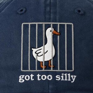 May include: A dark blue baseball cap with a white duck in a cage and the text "got too silly" embroidered on the front.