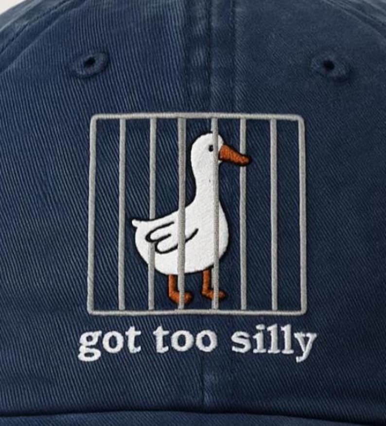 May include: A dark blue baseball cap with a white duck in a cage and the text "got too silly" embroidered on the front.