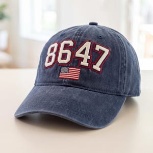 May include: A navy blue baseball cap with the number "8647" in white with red trim, and a small American flag. The hat is made of a soft, worn material.