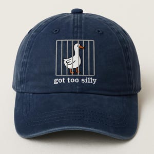 May include: A navy blue baseball cap with a white goose in a cage graphic and the text "got too silly".
