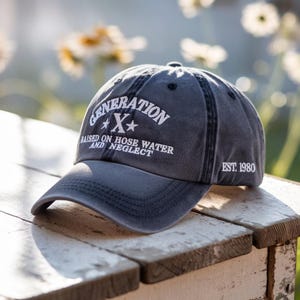 May include: A gray baseball cap with the text "GENERATION X" in white, along with the phrases "RAISED ON HOSE WATER AND NEGLECT" and "EST. 1980". The cap is sitting on a weathered wooden surface.