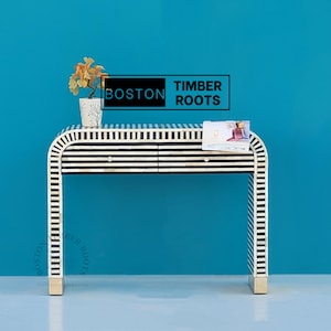 May include: A black and white striped console table with two drawers. The table is made of bone inlay and has a modern design. The table is sitting on a light blue background. The text "BOSTON TIMBER ROOTS" is visible in the image.