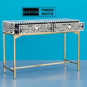 May include: A black and white bone inlay desk with two drawers and a gold metal frame. The desk has a floral design and the text "BOSTON TIMBER ROOTS" is visible on the top.