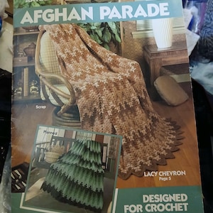 May include: A vintage crochet pattern book titled "AFGHAN PARADE" by Leisure Arts. The cover shows a brown and cream chevron-patterned afghan draped over a chair, with a smaller image of a green and black afghan. The text "DESIGNED FOR CROCHET" is also visible.