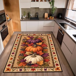 May include: A rectangular kitchen rug featuring a central design of three stacked pumpkins in purple, orange, and white, surrounded by colorful autumn leaves, berries, and vines. The rug has a decorative border with a repeating leaf pattern.