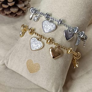 Peut inclure: Deux bracelets à breloques en argent et en or avec des breloques en forme de cœur. Les breloques sont décorées de strass scintillants.