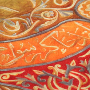 Pu&ograve; includere: Primo piano di un tessuto colorato con motivi intricati e calligrafia araba in oro. Il tessuto &egrave; un mix di colori arancio, rosso e oro.