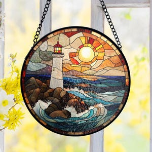 Puede incluir: Arte de ventana de vidriera redonda que representa un faro en una costa rocosa con una puesta de sol. El faro es blanco con la parte superior roja, sobre un cielo y un océano coloridos. La pieza está enmarcada en negro y cuelga de una cadena.