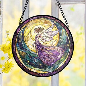 Può includere: Vetrata rotonda raffigurante una fata in abito viola e ali. Il design include un sole giallo, stelle e un bordo scuro, sospeso da una catena nera. L'opera d'arte evoca una scena celeste, ideale per l'arredamento della casa.