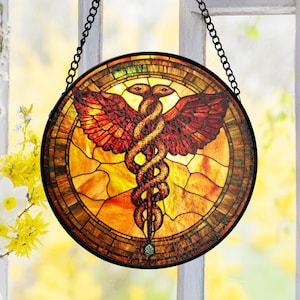 May include: Round stained glass panel featuring the Caduceus symbol, with two snakes entwined around a staff and wings. The panel has a black metal frame and a hanging chain. The colors are warm, with shades of red, orange, and yellow.