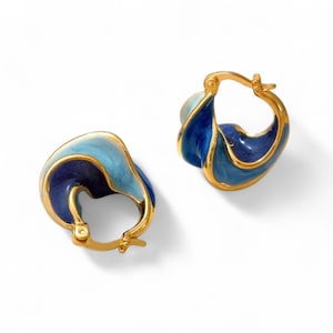 May include: A pair of gold hoop earrings with blue and light blue enamel. The earrings are shaped like a wave and have a twisted design.