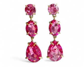 May include: A pair of dangle earrings with three pink gemstones on each earring. The top gemstone is round, the middle gemstone is oval, and the bottom gemstone is pear-shaped.