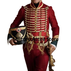 Puede incluir: Un uniforme militar burdeos con adornos dorados, botones y bordados. El uniforme incluye una chaqueta, pantalones y un sombrero. La chaqueta tiene múltiples filas de botones y adornos dorados. El sombrero es negro con detalles dorados.