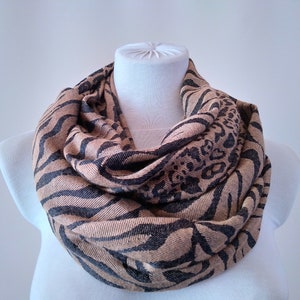 Puede incluir: Una bufanda infinita marrón y negra con estampado de cebra y leopardo.