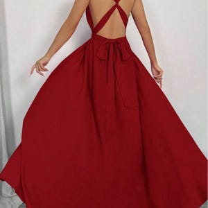 Pu&ograve; includere: Un abito lungo color rosso cremisi con schiena incrociata e fiocco in vita. L'abito presenta una gonna fluida e uno scollo all'americana. Il design senza schienale aggiunge un tocco di eleganza a questo abito da sera.