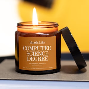 以下が含まれることがあります： 黒い蓋が付いた茶色のガラス瓶に入った、火の灯ったキャンドル。「Smells Like COMPUTER SCIENCE DEGREE」と書かれたラベルが付いています。背景は黄色です。