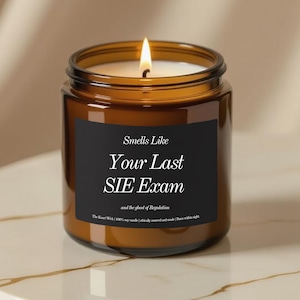 Può includere: Un barattolo di candela in vetro marrone acceso con un'etichetta nera che recita "Smells Like Your Last SIE Exam". La candela è appoggiata su una superficie bianca e dorata. La candela ha cera bianca e uno stoppino acceso.