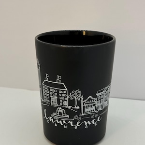May include: Black ceramic mug with a white illustration of a city skyline and the text "Lawrence Kansas".