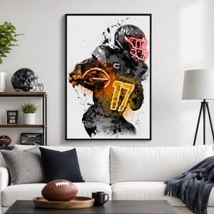 May include: A framed vertical wall art print featuring a stylised black and white watercolour illustration of a football player in a helmet and jersey with the number 17 and the text COMMANDERS in glowing neon orange and red accents.