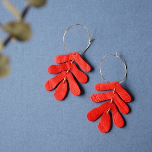 May include: A pair of red leather earrings with a gold hoop and a leaf-shaped design.