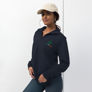 May include: A navy blue quarter-zip sweatshirt with the text "CAN GO ROGUE" in green and orange. The sweatshirt has a small green logo on the chest and is paired with a beige baseball cap.
