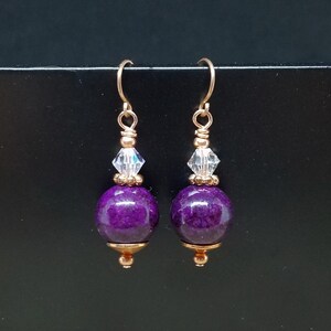 Puede incluir: Pendientes de piedra preciosa púrpura con detalles dorados y cuentas de cristal transparentes.