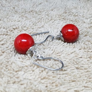 May include: A pair of red bead earrings with silver hooks. The beads are round and have a slightly textured surface.