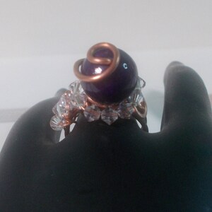 May include: A ring featuring a purple gemstone, clear crystal accents and copper wire wrapping.