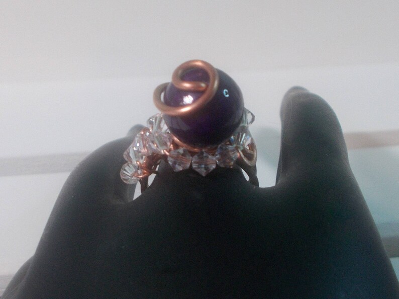 May include: A ring featuring a purple gemstone, clear crystal accents and copper wire wrapping.