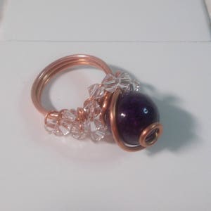 May include: A copper wire ring with a purple bead and clear crystal beads.