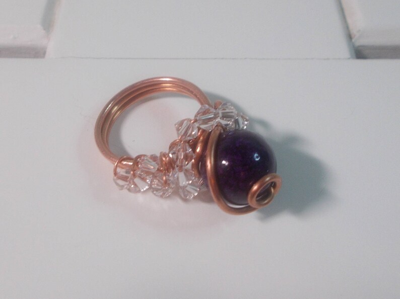 May include: A copper wire ring with a purple bead and clear crystal beads.