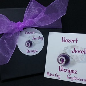 May include: A purple and white jewellery box with a purple ribbon and a white label that says "Dezert Jewellery Dezignaz Helen Coy hcoyl@cox.net"