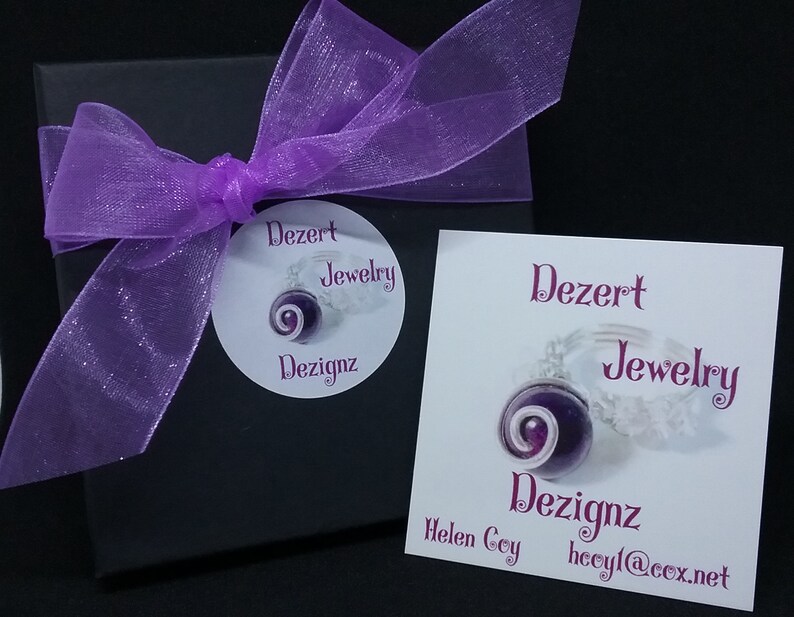May include: A purple and white jewellery box with a purple ribbon and a white label that says "Dezert Jewellery Dezignaz Helen Coy hcoyl@cox.net"