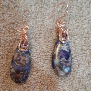 May include: A pair of teardrop-shaped earrings with a copper wire design and a blue and purple stone.