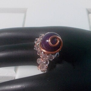 May include: A purple gemstone ring with a copper wire design and clear crystal accents.