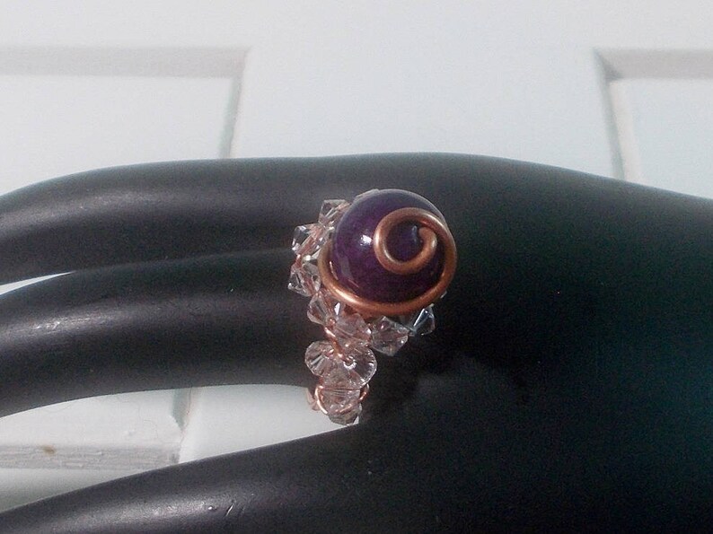 May include: A purple gemstone ring with a copper wire design and clear crystal accents.