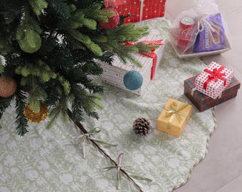 Puede incluir: Un árbol de Navidad decorado con adornos y una falda de árbol floral verde. Varios regalos envueltos en rojo, blanco y dorado están dispuestos alrededor del árbol. Una bolsa transparente contiene una lata de Coca-Cola y un paquete de galletas.
