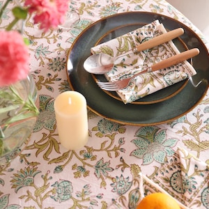 Puede incluir: Una mesa puesta con un plato verde oscuro, una servilleta doblada con un dise&ntilde;o floral verde y cubiertos con mangos de madera. Una vela encendida y un jarr&oacute;n con flores rosas se encuentran sobre un mantel floral.